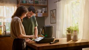 A man and a woman standing over a kitchen bench looking at their Thermomix.